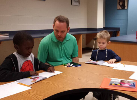 A male teacher sitting with students at a desk