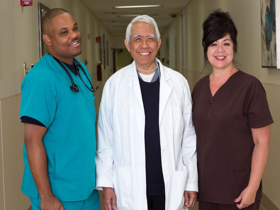 Three Beverly Hospital staff members standing and smiling in the hallway.