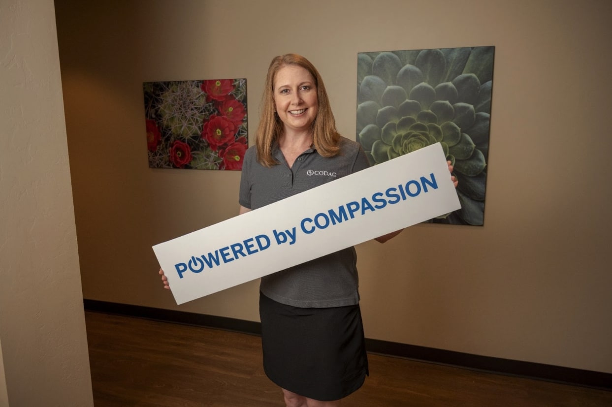 CODAC's employee holding a ribbon with 'Powered by Compassion' text on it