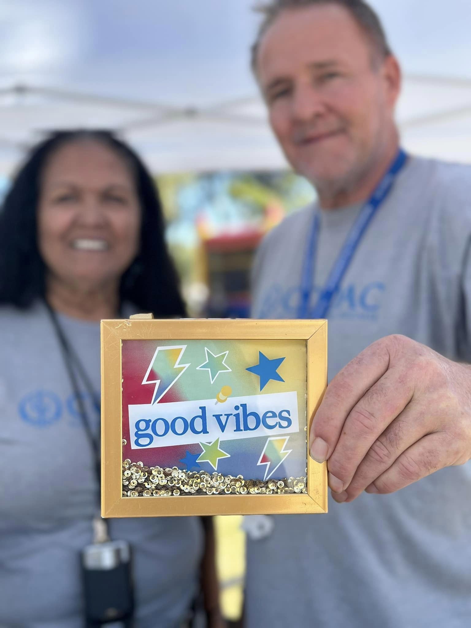 2 people holding a souvenir having the word 'good vibes'