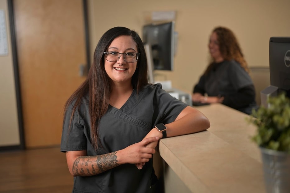 A woman in medical scrubs stands at a counter, engaged in her work environment, showcasing professionalism and care.